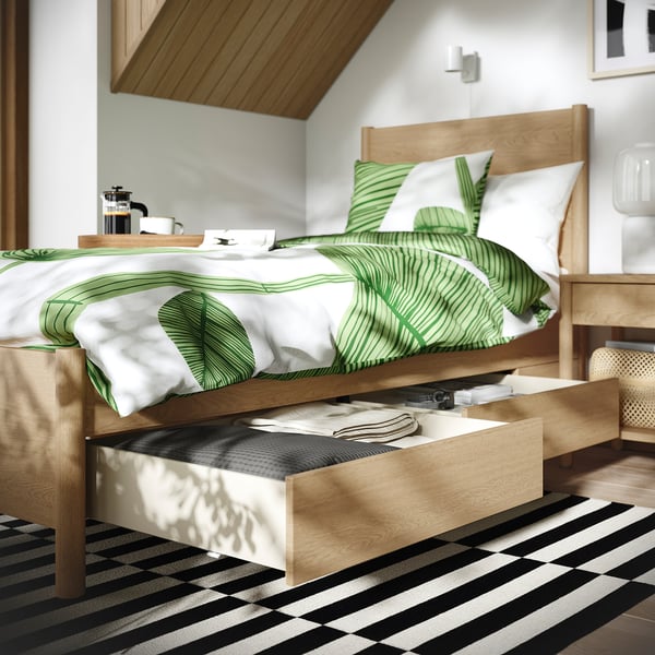 Bed with green and white bedding, wooden headboard, two open drawers underneath.