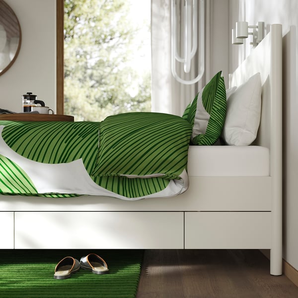 Bed with green striped pillows and white drawers.