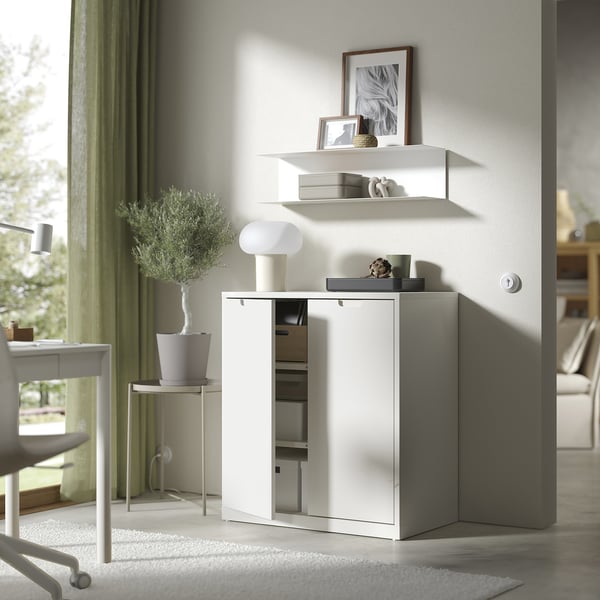 Modern white cabinet with adjustable shelves and soft-closing doors, decorated with a lamp, plant, and framed items.