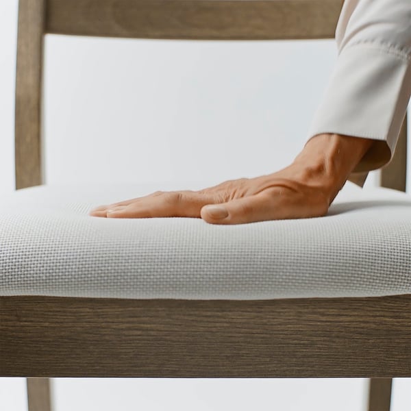 Hand pressing firmly on cushioned seat of modern chair, showcasing comfort and quality control.