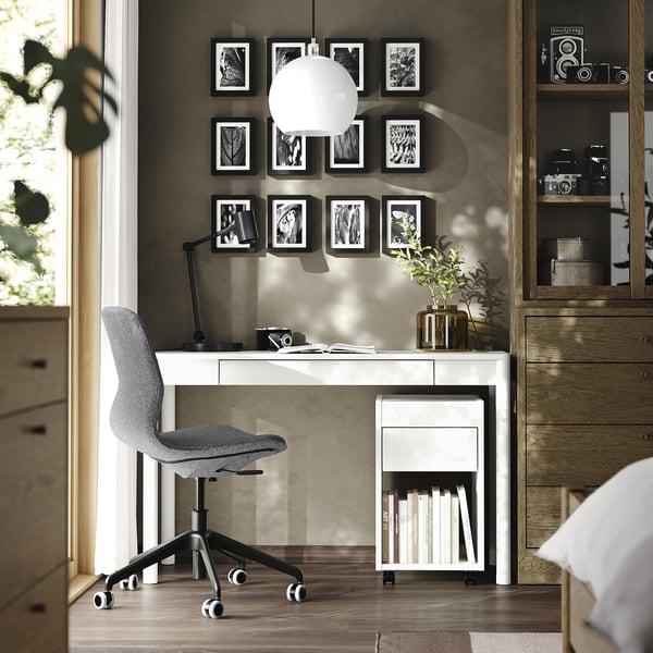 Modern home office with white TONSTAD desk, grey chair, wall art, and wooden cabinet.