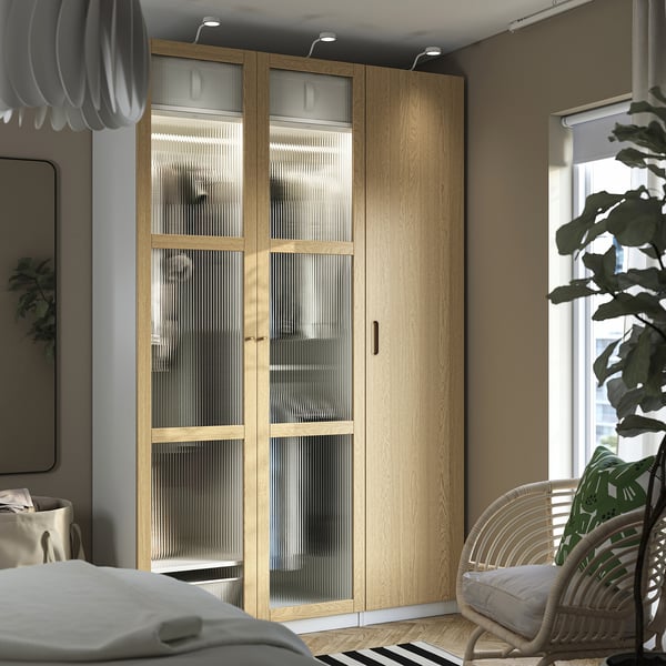 Modern bedroom with TONSTAD wooden wardrobe, sliding doors, wicker chair, pendant light, bed, & small table lamp.