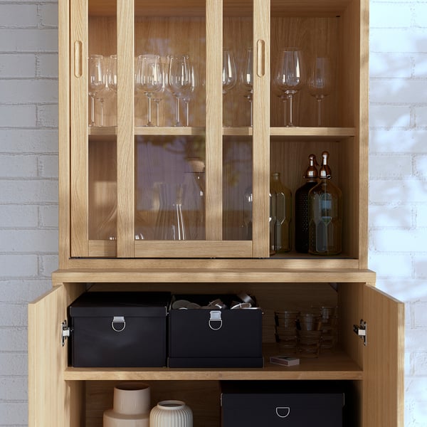 Cabinet with glass doors displays wine glasses and bottles. Lower shelves hold storage boxes and vases.