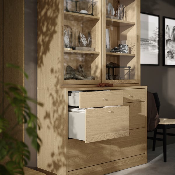 Light wood cabinet with open drawers and glass doors showcasing decorative items.