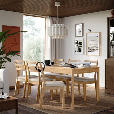 Modern dining space with TONSTAD table, oak, cushioned chairs, window, art, plant, lamp.