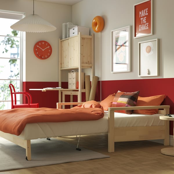 Cosy bedroom with TORNSBORG sofa bed, red clock, wooden shelves, orange pillows, and colourful art prints.