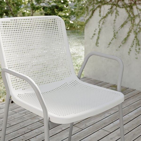 Two white plastic chairs on wooden deck, one angled slightly behind the other, surrounded by greenery.