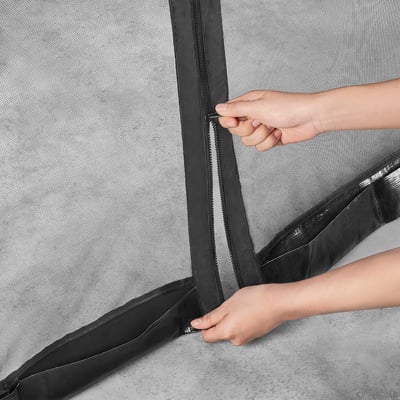 A person is zipping shut a TORPÖN insect net, which attaches to a parasol, creating a sealed, insect-free space.