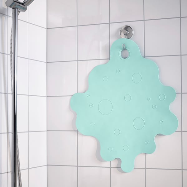 A light green, non-slip bath mat hangs on a white tiled shower wall. Suction cups secure it in place for safety.