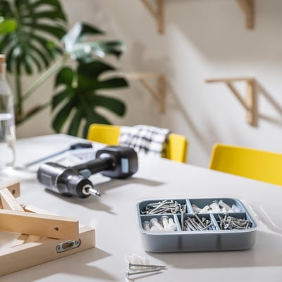 Latched toolbox with screws, drill, and plant on a white table.