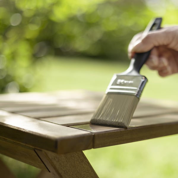Applying transparent wood stain on outdoor furniture using a brush.
