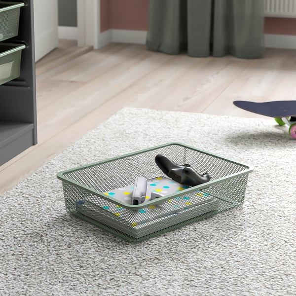 Mesh storage bin on carpet holding gaming controllers and accessories. Part of TROFAST series for organizing items.