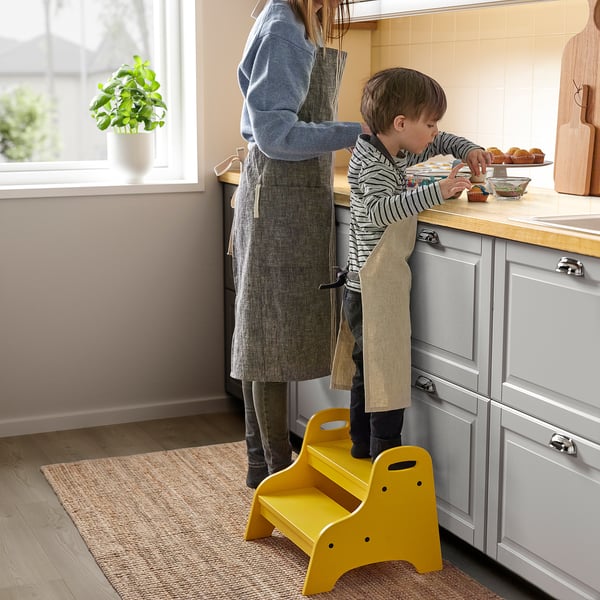 Child on stool reaches for cupcakes in kitchen.