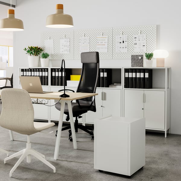 Modern office featuring TROTTEN white storage cabinet with black mesh chair and light wood desk. Organised with binders, plants, and pendant lights.