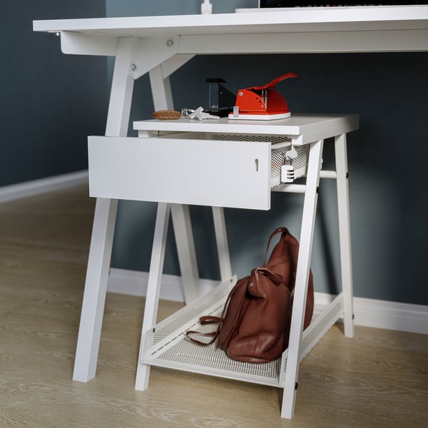 Modern white desk with shelf, drawer, red stapler, brown bag, blue wall.