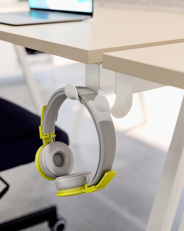 Grey and yellow headphones hang on a white hook under a desk.