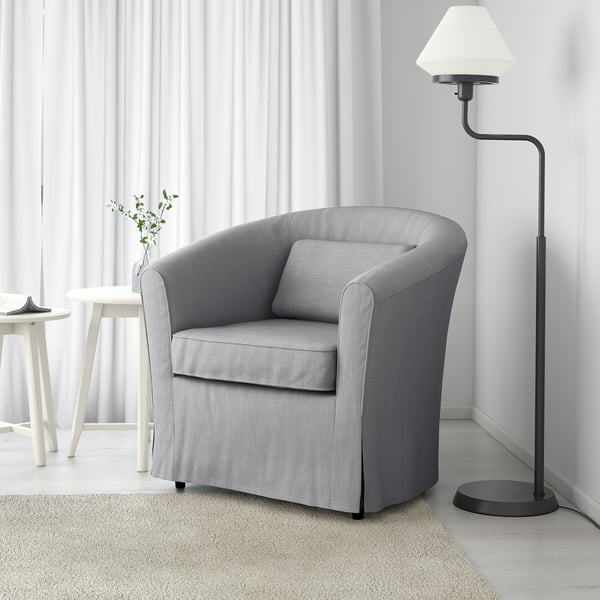 A grey upholstered chair with a cushion, positioned for comfort, in a minimalist room with a floor lamp and a side table.