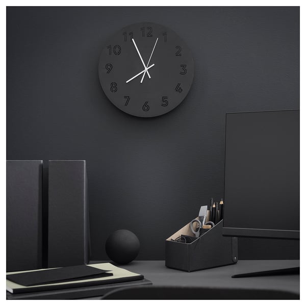 Modern black office setup. Black round clock with white hands on a dark wall. Black desk with black accessories.