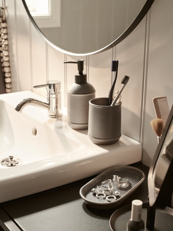 Modern bathroom sink with round mirror reflecting toothbrush holder and soap dispenser. Sleek design.