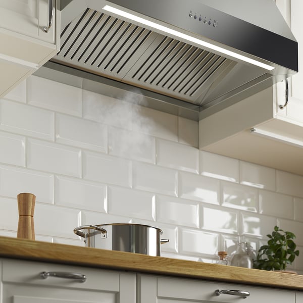 Modern stainless-steel range hood over stove, with led lights on, effectively ventilating steam from cooking.