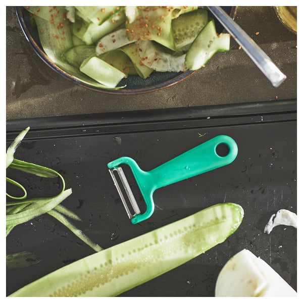Green peeler on counter with peeled cucumbers.