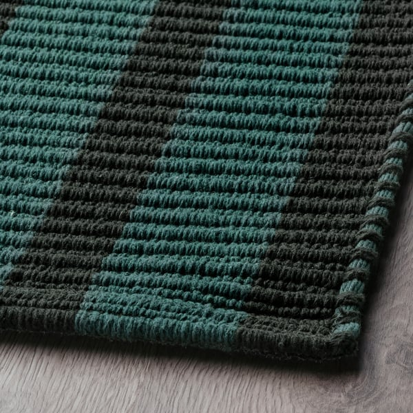 Dark green and black striped rug, texture visible, on wooden floor.