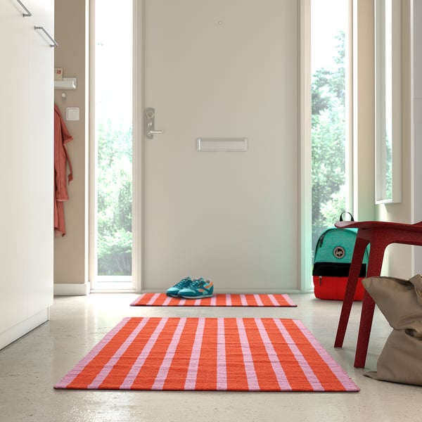 Bright pink & orange striped rug near door, smaller than chair and bag.