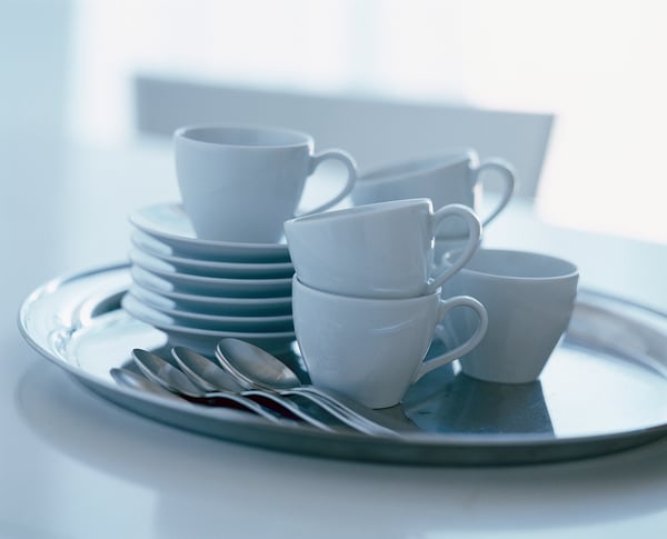 Stacked white porcelain cups and plates on tray with spoons, minimalist and durable design.