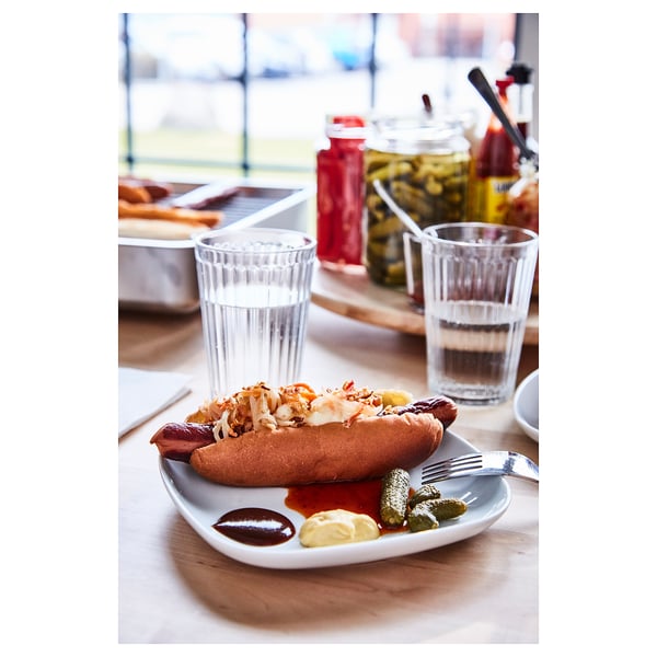 Plate with hot dog and condiments, glasses, and bottles on wooden table.