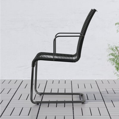 Black modern outdoor chair with high back and armrests for comfort, placed on tiled patio.