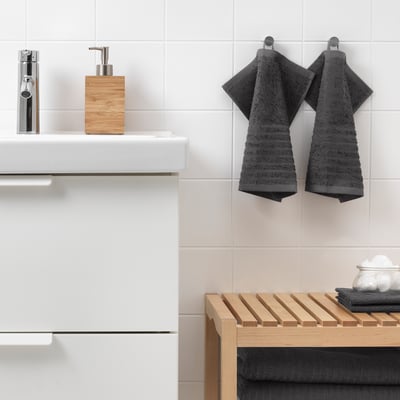 Modern bathroom with white sink, chrome tap, dark grey VÅGSJÖN towels, wooden soap dispenser, and slatted shelf.