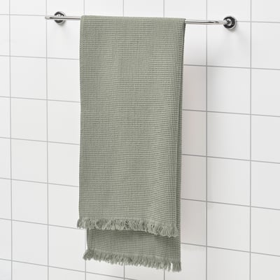 Green VALLASÅN towel on silver rod against white tiles, textured with fringe.