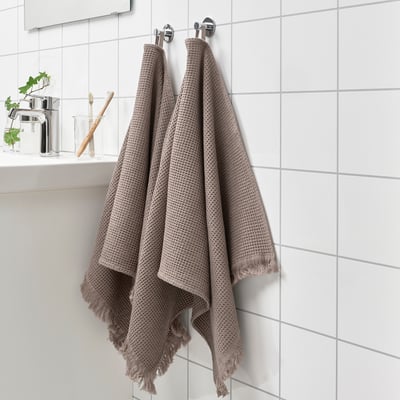 Two hanging gray towels with waffle texture and fringe edges on bathroom wall, near toiletries.