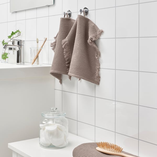 Bathroom with white tiles and two VALLASÅN towels. One folded with cotton rounds, brush beside. Absorbent, quick-drying waffle towels.