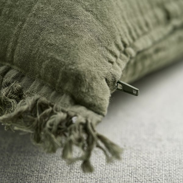 Faded green cushion cover with frayed edges and zip, showcasing soft cotton texture.