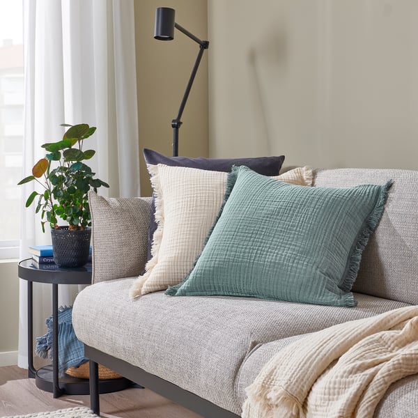 Cosy living room with beige sofa, VALLKRASSING cushions, throw, side table with plant, natural light, relaxed vibe.