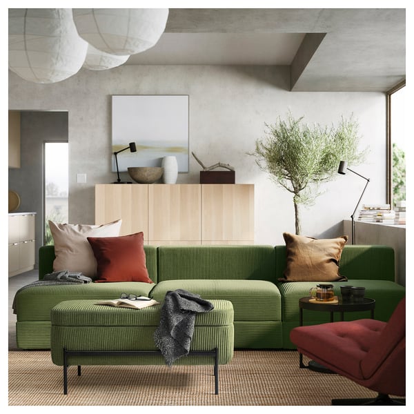 Modern living room with green VALTORP sectional sofa, wooden sideboard, red chair, large plant, rug, and pendant lamps.