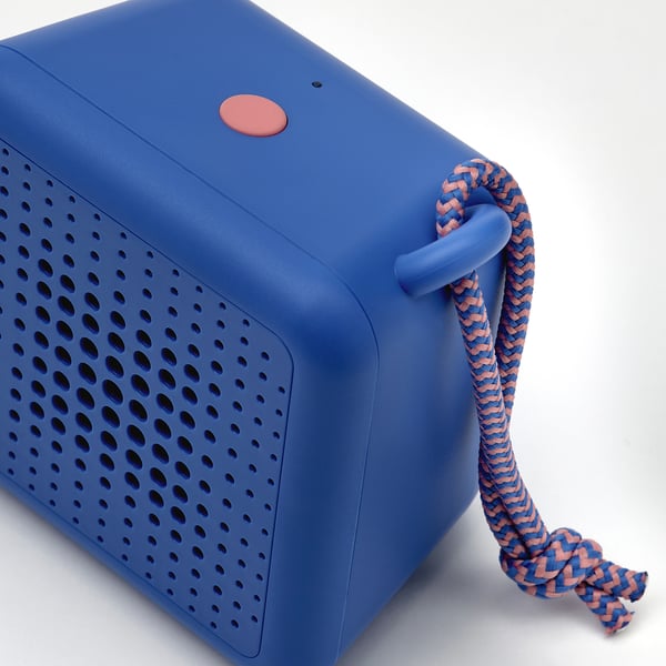 Blue portable speaker with rope handle, textured surface, and round power button.