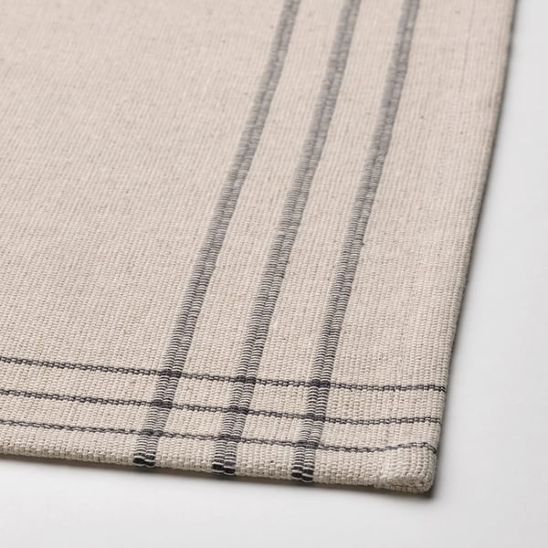 Beige striped place mat, woven from cotton and jute, displayed on a white surface.