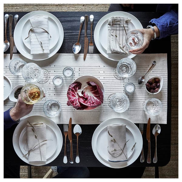 Table set with VÅRARV runner, plates, glasses, cutlery, napkins, red cabbage dish, two people with drinks.