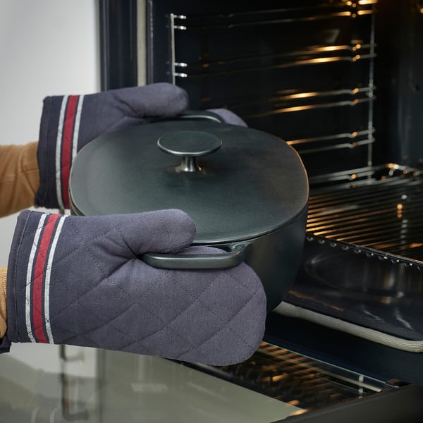 Hand with oven mitt removes cast iron casserole from oven. Oven mitt protects from heat.