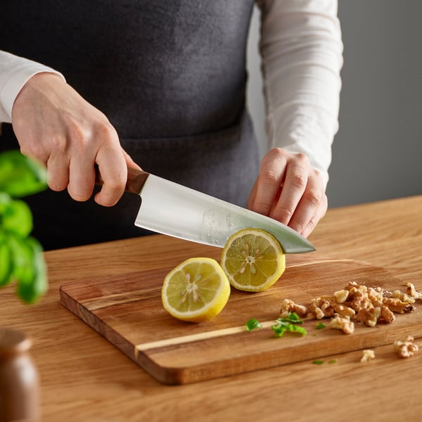Person slicing lemon on wooden cutting board with knife.