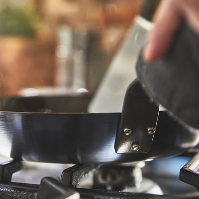 Hand lifts large metal pan with two bolts, likely for cooking.