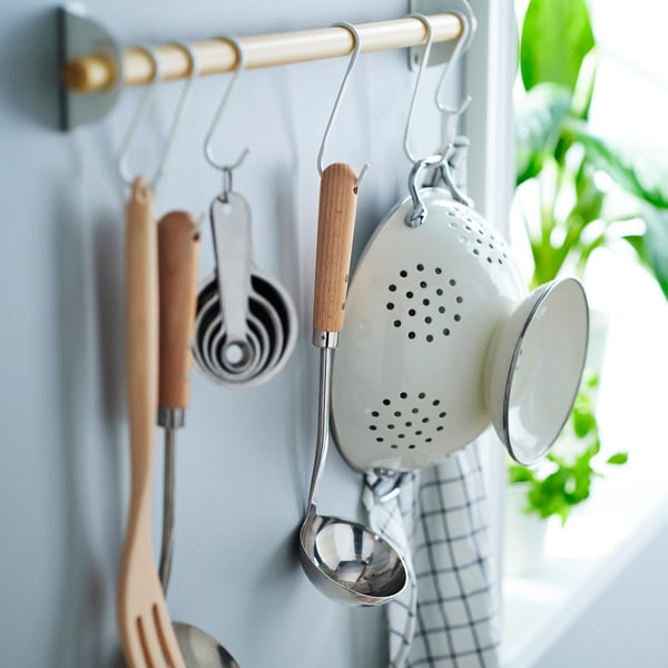 A kitchen ladle with a wooden handle hangs from a hook, part of the VARDAGEN series.