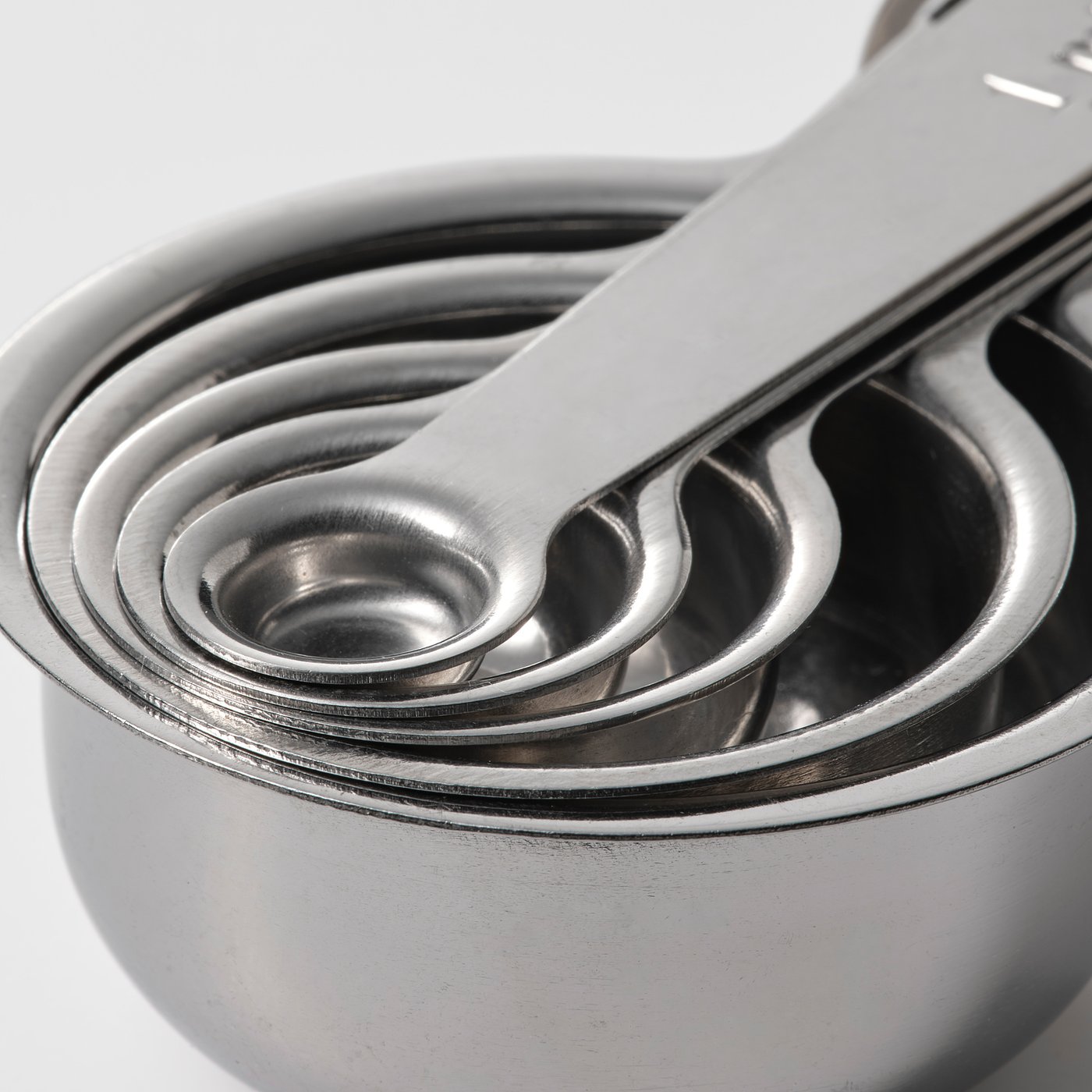 Five stacked stainless steel measuring cups, polished and gleaming, nested neatly together for compact storage.