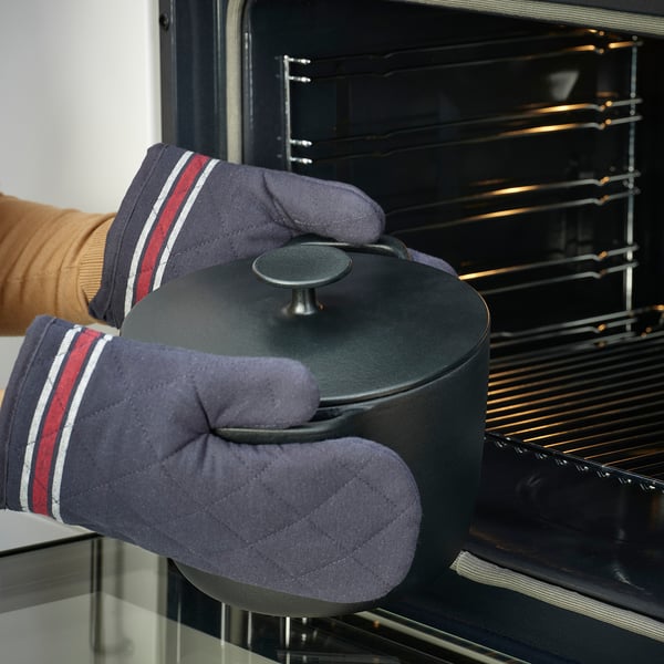 Person wearing oven mitts places black cookware into oven. The cookware evenly distributes heat.