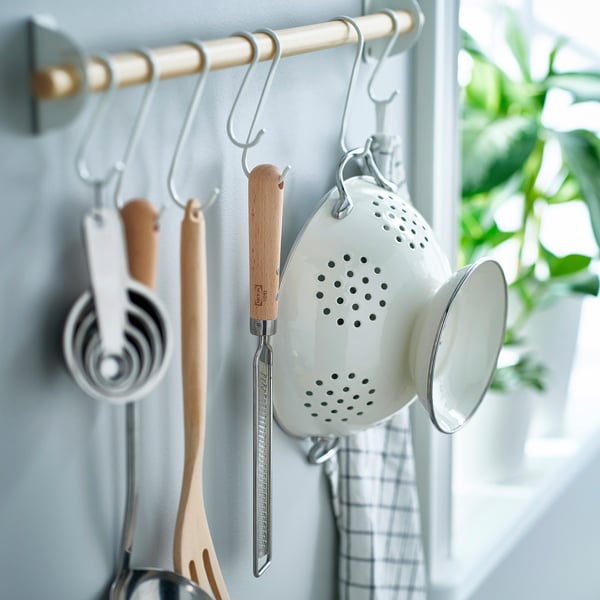 Kitchen utensils hung on hooks. A white zester with wooden handle, measuring cups, wooden spatula, and white colander are visible.