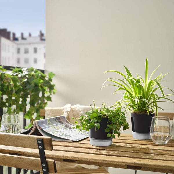 Patio scene with VÅRDTRÄD self-watering pots, plants, glasses, and magazine.