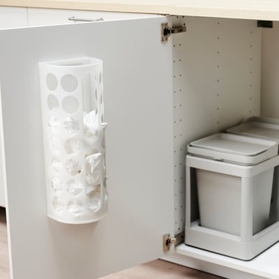 A white plastic bag organiser hangs inside a cabinet door, storing multiple crumpled plastic bags and keeping them neat and accessible.