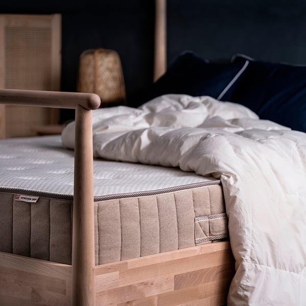 Cosy bed with white VATNESTRÖM mattress, navy pillows, wooden frame, soft lighting.